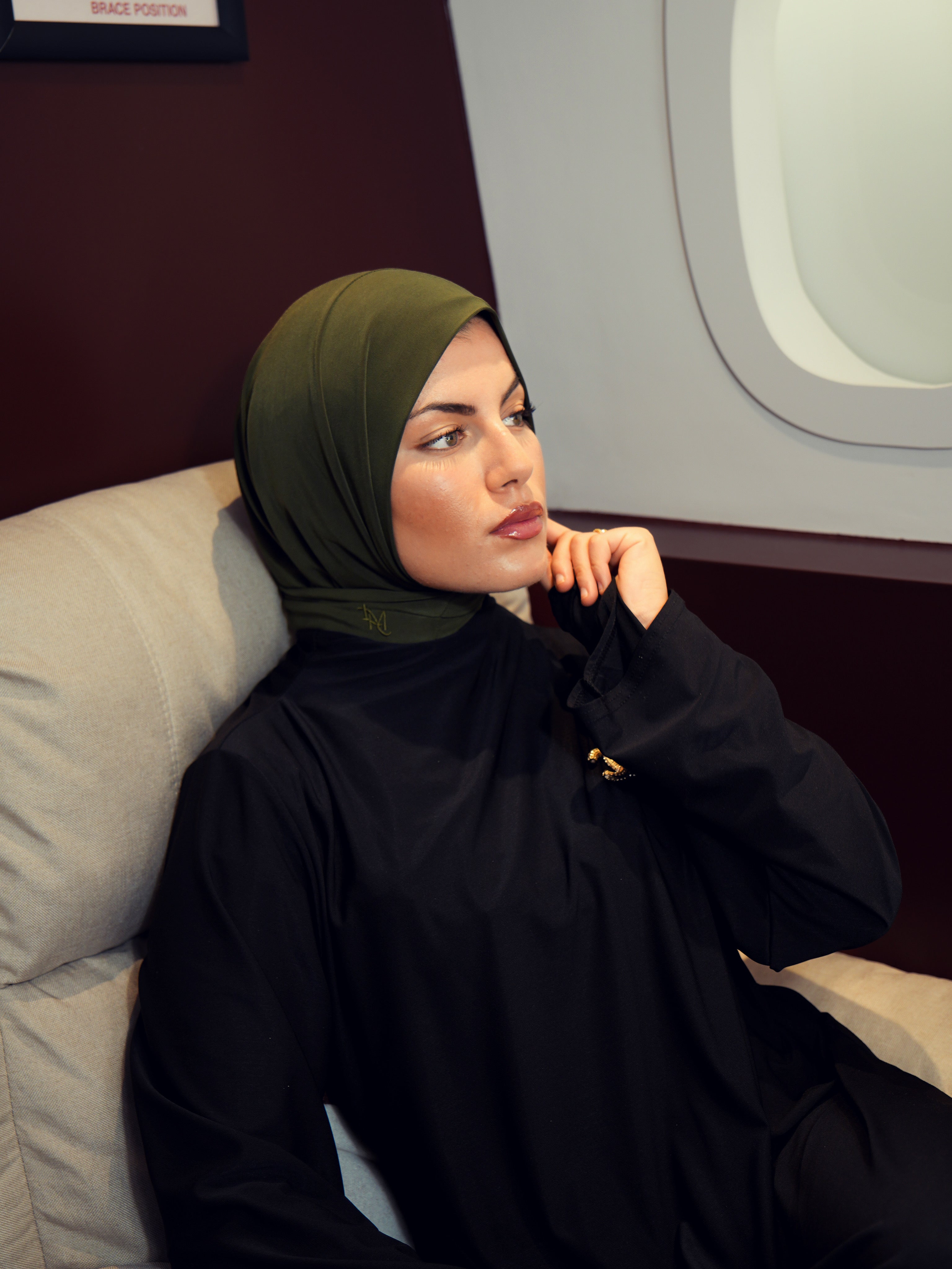 Woman wearing a instant hijab and black outfit sitting on an airplane.
